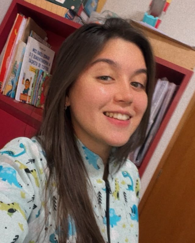 Isabella sorrindo no consultório, com uma estante de livros e jogos infantis ao fundo.